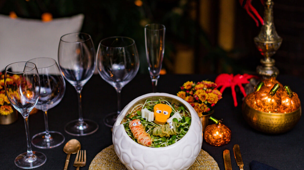 theme-07 Halloween-themed dinner table setting featuring a white cauldron bowl filled with microgreens, a skull garnish, and edible mummies.