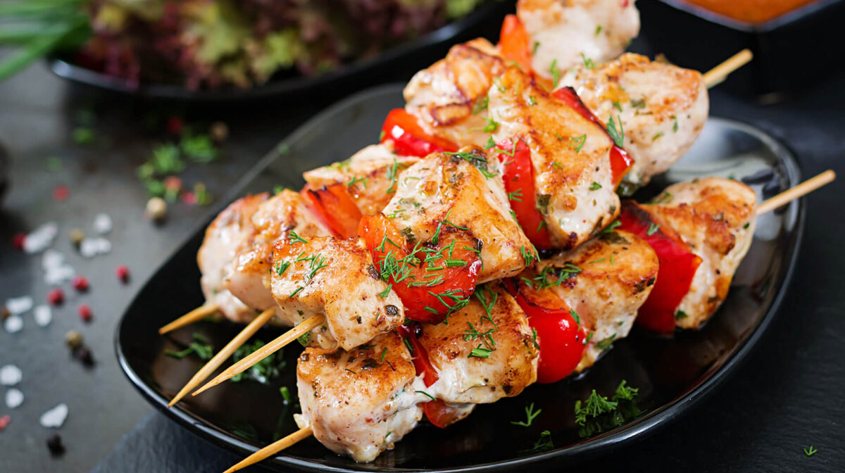 theme-08 Grilled chicken skewers with red bell peppers and fresh dill garnish on a black plate.