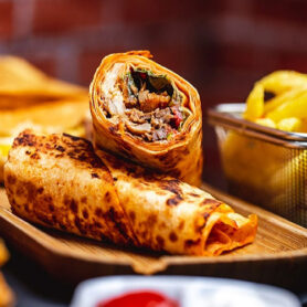 Gourmet grilled chicken wrap sliced on a wooden platter with a side of crispy golden fries