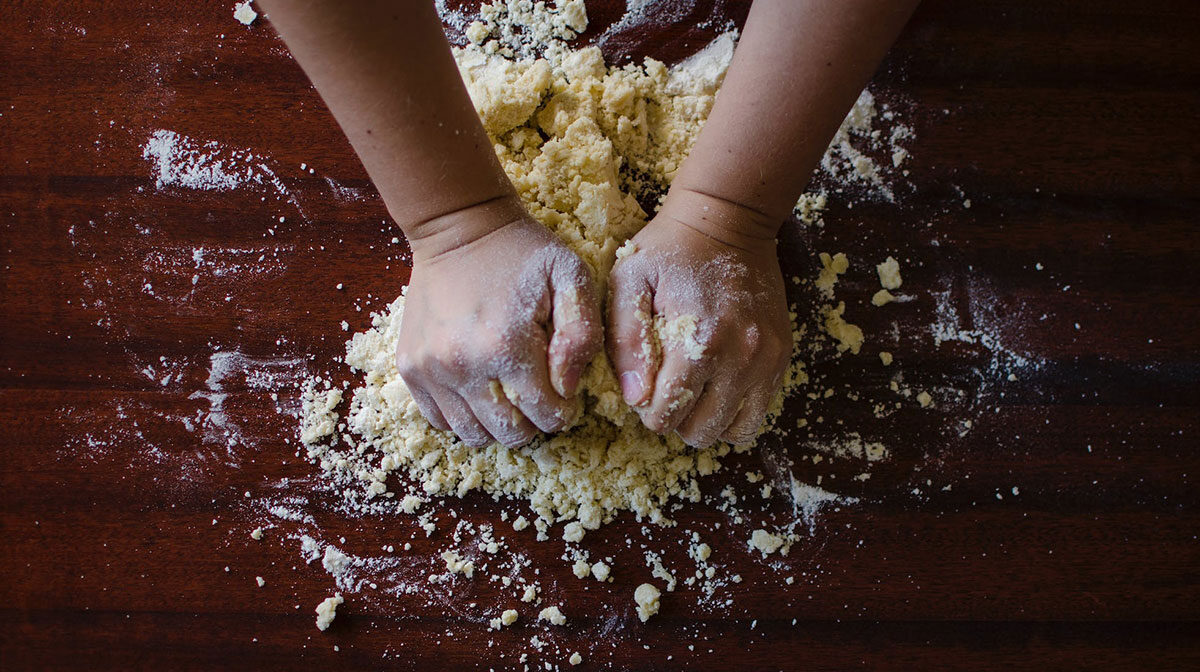 h4-blog3 Close-up of the bread-making process with hands kneading flour and dough on a dark textured background