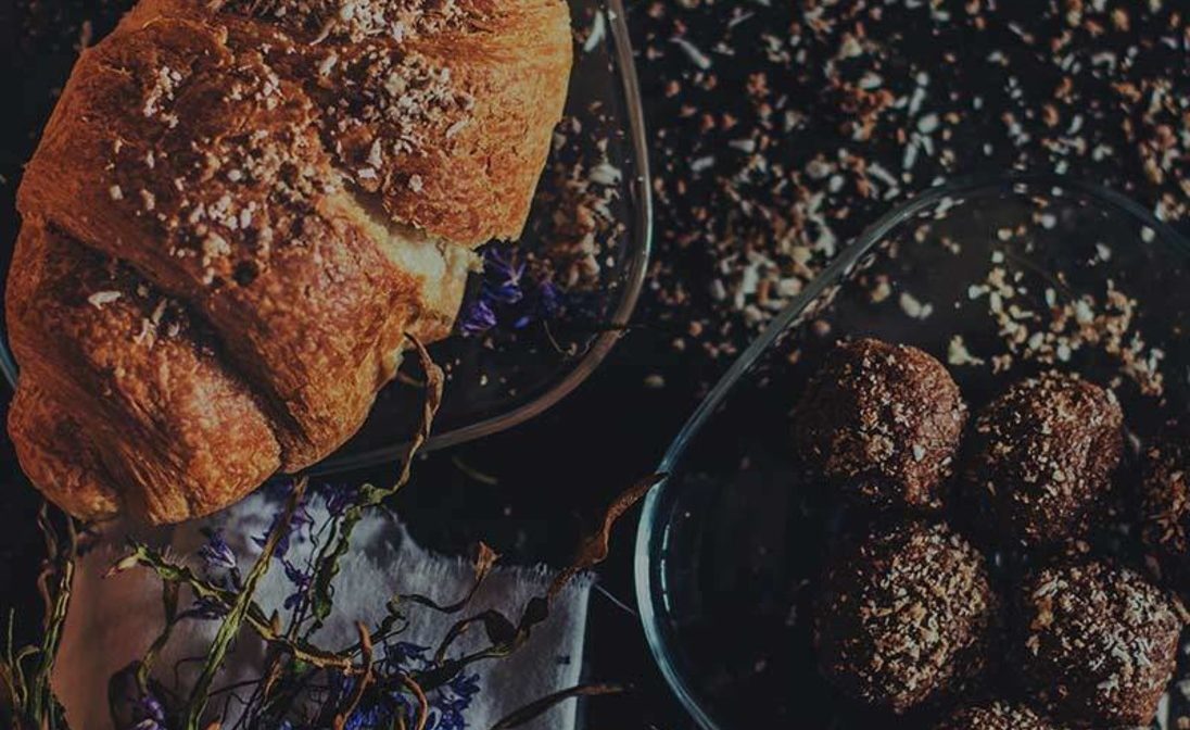 h4-blog4 Gourmet croissant and decadent chocolate truffles displayed on a dark textured surface for a minimalist bakery catalog