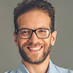 Professional headshot of a smiling male entrepreneur with glasses and a beard, featuring a modern and approachable aesthetic.