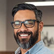 A professional headshot of an entrepreneur with glasses and a beard, featuring a modern and approachable aesthetic.